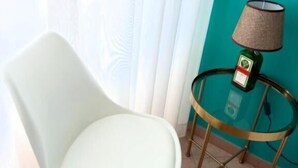 A white chair with a cushioned seat, a small round table with a lamp, and a teal-colored wall. - B&B Napoli Tonic (Naples)