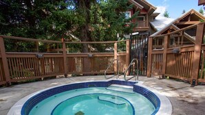 Un jacuzzi circular con baldosas azules, rodeado por una terraza de madera y una valla.
