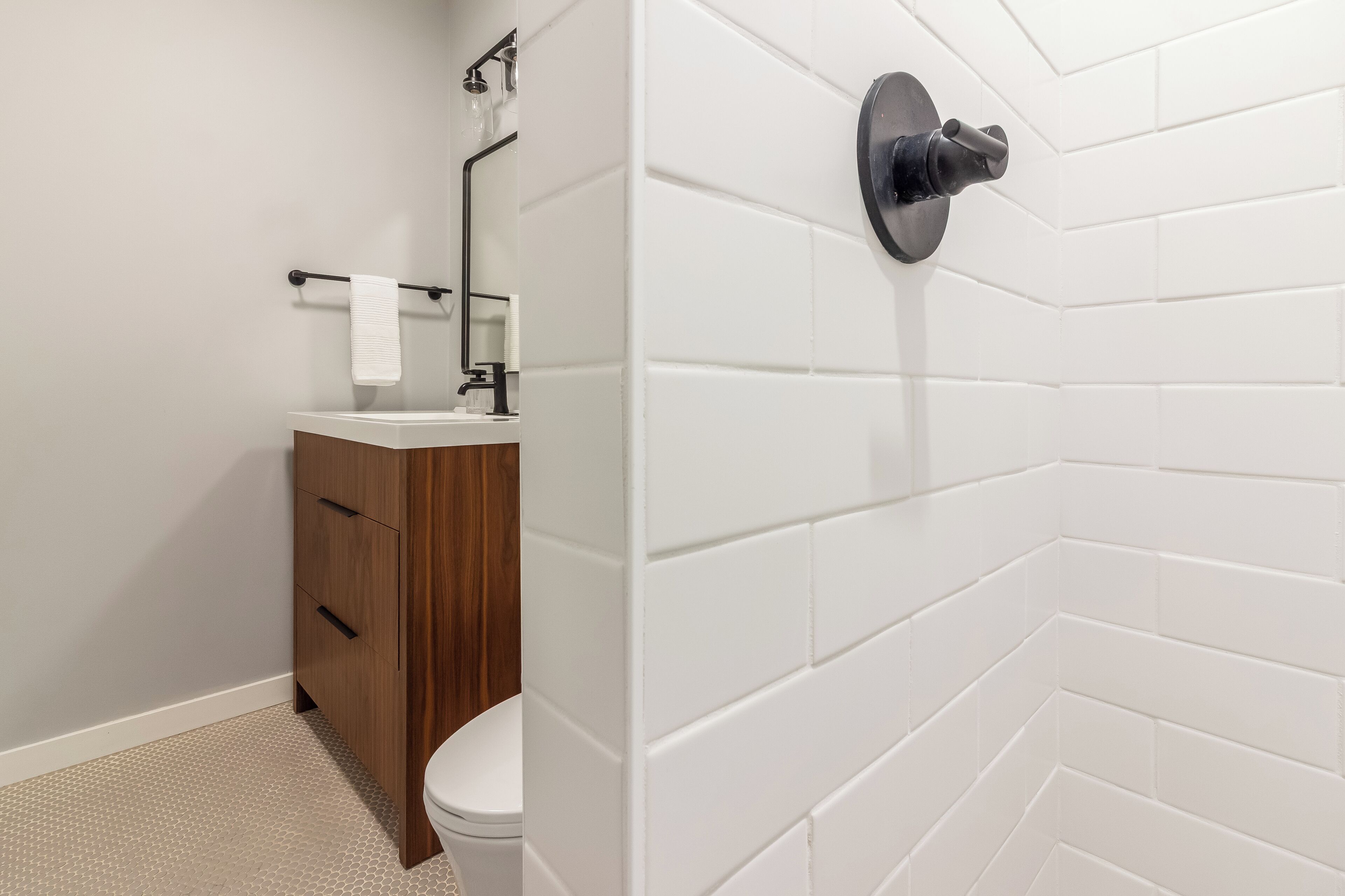 A modern bathroom with a white tiled shower wall, a wooden vanity with a sink, and a toilet.