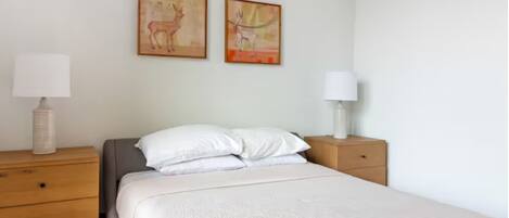 A bedroom with a bed, two nightstands, and two wall-mounted lamps.