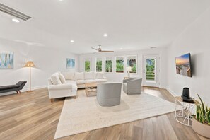 Uma sala de estar moderna com um sofá branco, poltronas cinzas, uma mesa de centro e um tapete grande.
