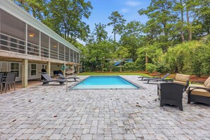 A pool area with lounge chairs, a covered seating area, and a view of the surrounding greenery.