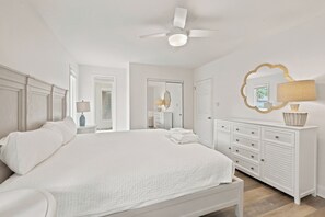 A bedroom with a large bed, a ceiling fan, a dresser, and a mirror.