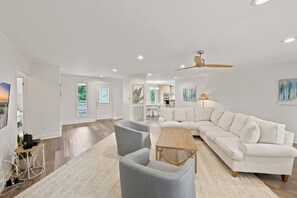 A spacious living room with a white sofa, grey armchairs, a wooden coffee table, and a ceiling fan.