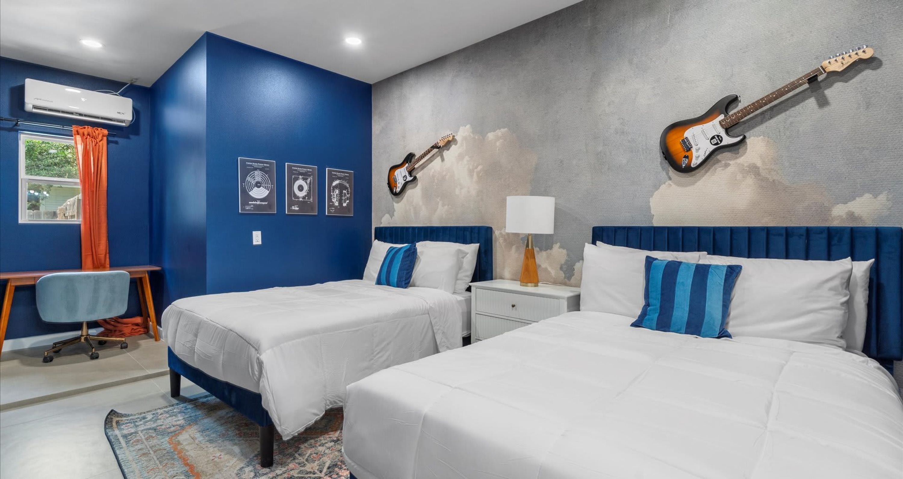 Une chambre d’hôtel avec deux lits, un bureau, un climatiseur et des guitares accrochées au mur.
