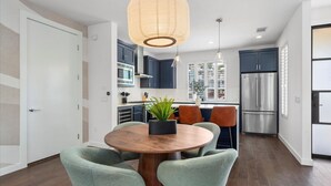 Eine moderne Küche mit dunklen Schränken, einem Edelstahlkühlschrank und einem Essbereich mit einem runden Holztisch und grünen Stühlen.