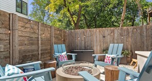 A backyard with a fire pit, two Adirondack chairs, and a wooden fence.