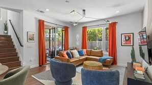 A modern living room with a brown leather sofa, blue armchairs, and a dining area with a wooden table.