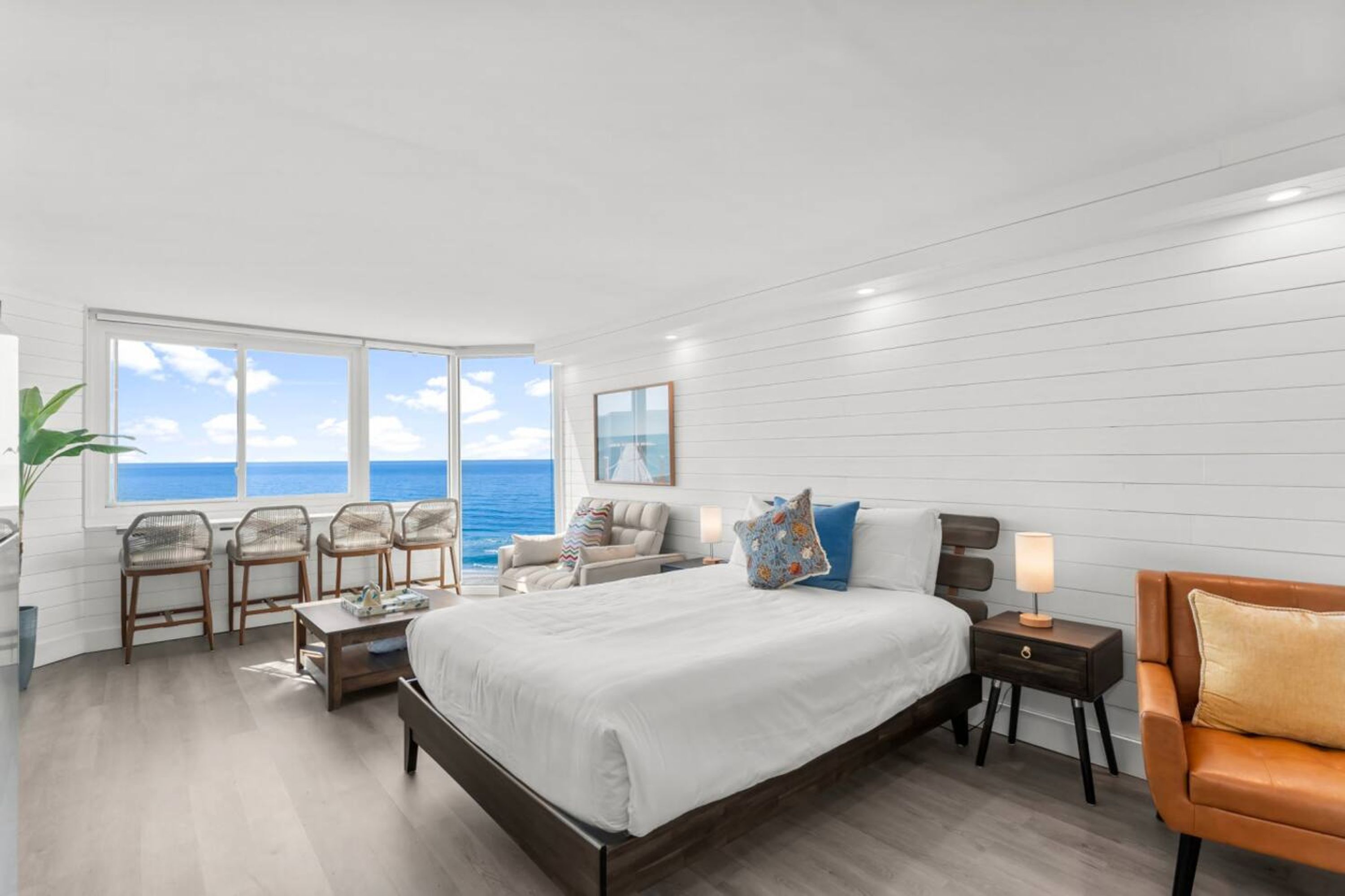 Una camera da letto con un letto grande, un angolo salotto con poltrone, un comodino e vista sull'oceano.