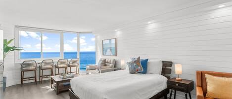 Una camera da letto con un letto grande, un angolo salotto con poltrone, un comodino e vista sull'oceano.