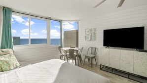 A bedroom with a large bed, a TV mounted on the wall, a dining table with chairs, and a view of the ocean through the windows. - Sea the Gulf - Top of the Gulf 809 - Luxury Resort (Panama City Beach)