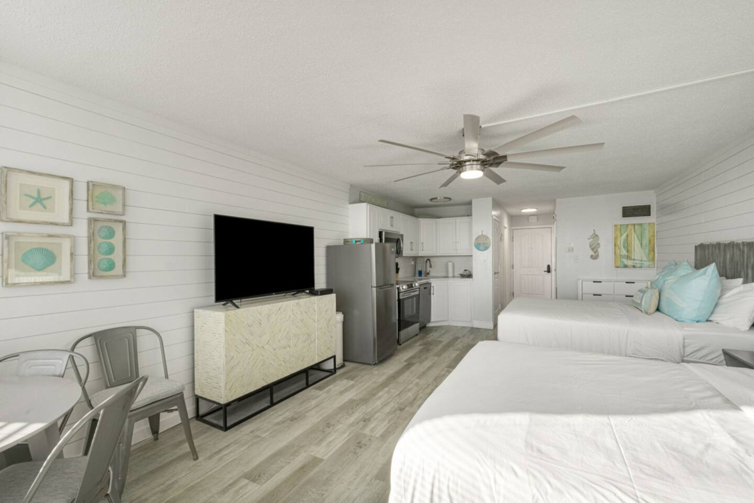 A modern hotel room with a kitchenette, a dining area, and a bedroom with two beds.