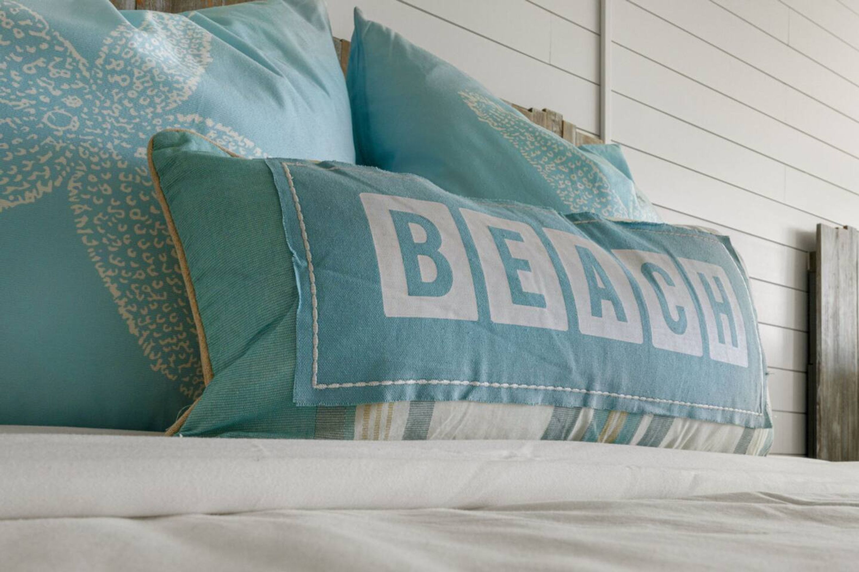 Una cama con almohadas turquesa, una de ellas con la palabra 'BEACH'.