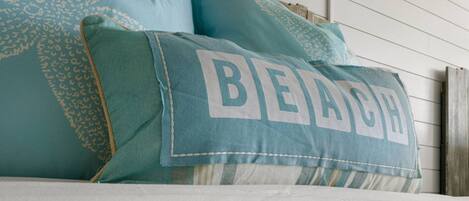 Una cama con almohadas turquesa, una de ellas con la palabra 'BEACH'.