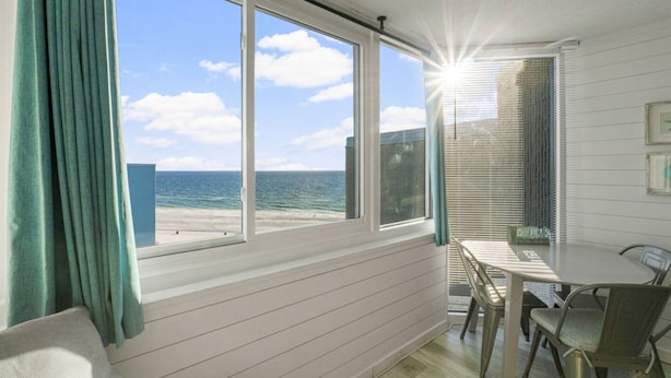 A room with a large window overlooking a beach, a table with chairs, and a view of the ocean. - Sea the Gulf - Top of the Gulf 809 - Luxury Resort (Panama City Beach)