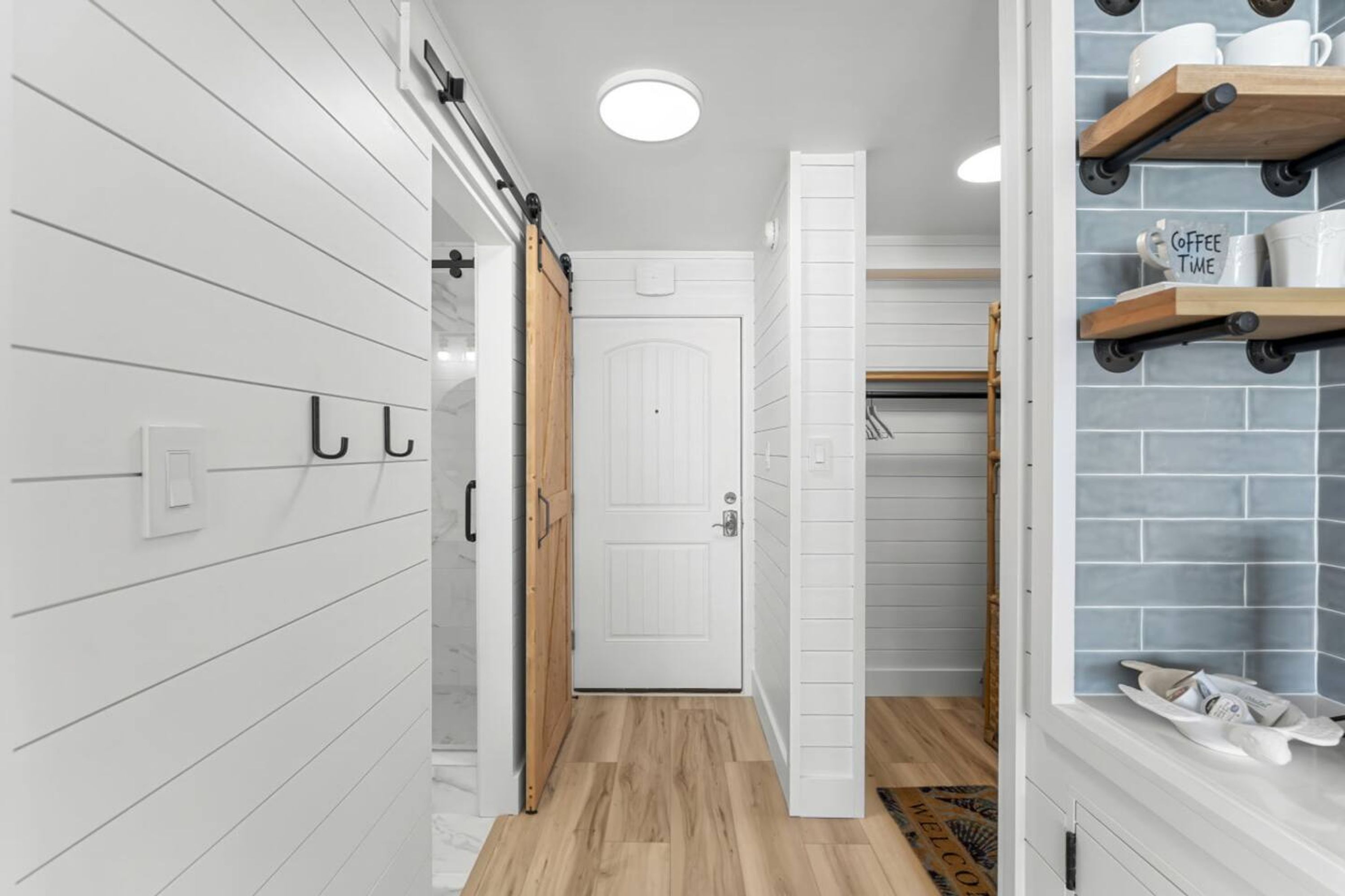 A modern bathroom with a white door, wooden floor, and a towel rack with a 'Coffee Time' sign.