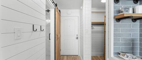 A modern bathroom with a white door, wooden floor, and a towel rack with a 'Coffee Time' sign.