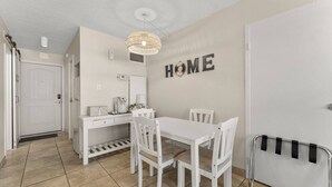 Ein heller Essbereich mit Tisch und Stühlen, eine weiße Tür und eine Wand mit dem Wort „HOME“.
