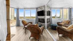 A modern living room with wicker furniture, a fireplace, and large windows offering a view of the city. - Top of the Gulf 620 Beachfront Couples Retreat (Panama City Beach)