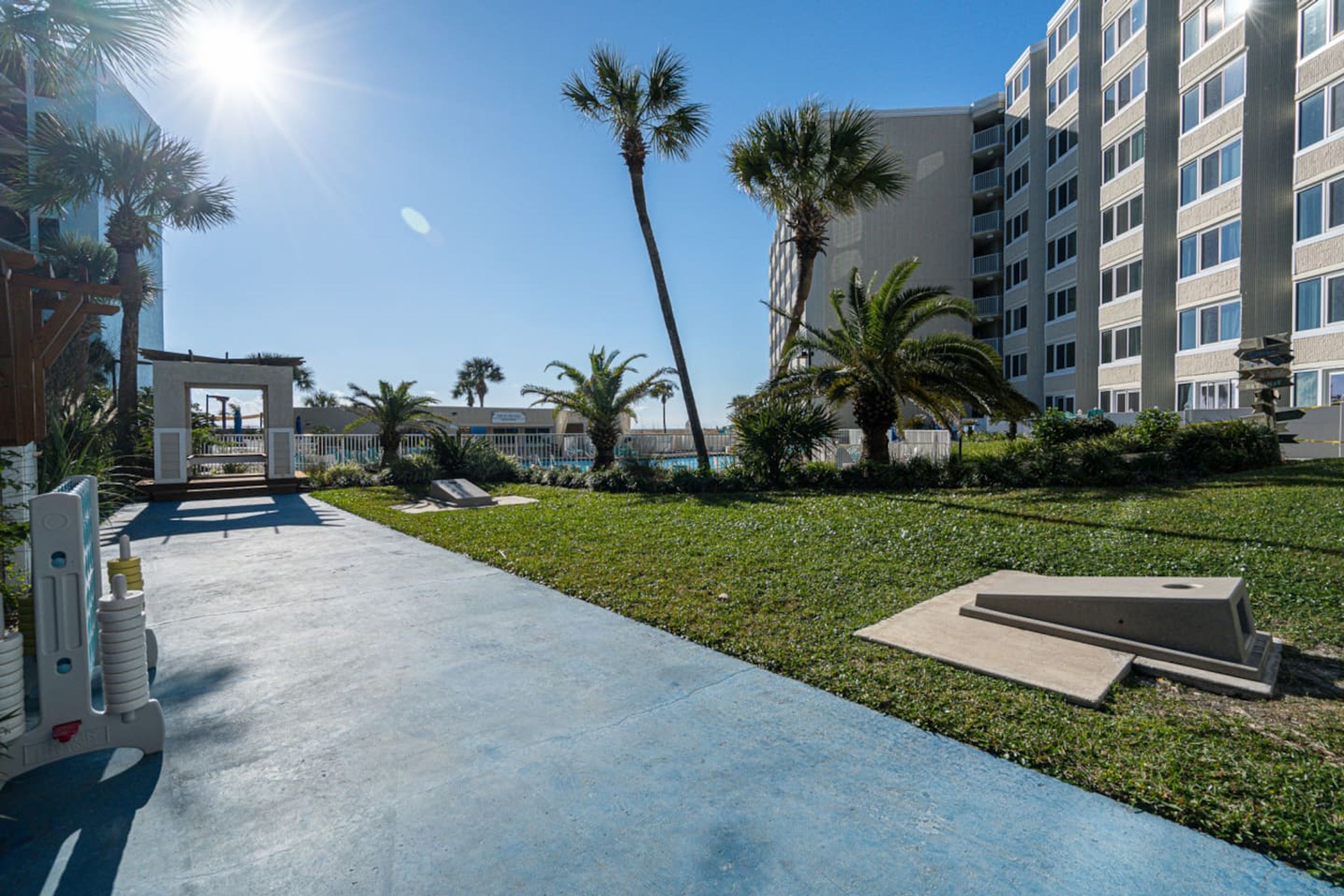 A courtyard with a concrete pathway, palm trees, and a building with multiple balconies.