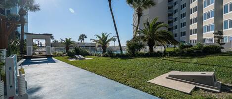 A courtyard with a concrete pathway, palm trees, and a building with multiple balconies.