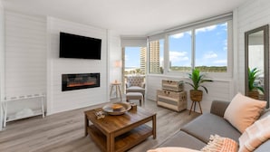 A modern living room with a fireplace, a flat-screen TV, a sofa, and a view of tall buildings. - Top of the Gulf 622 - Beach Front Condo Resort (Panama City Beach)
