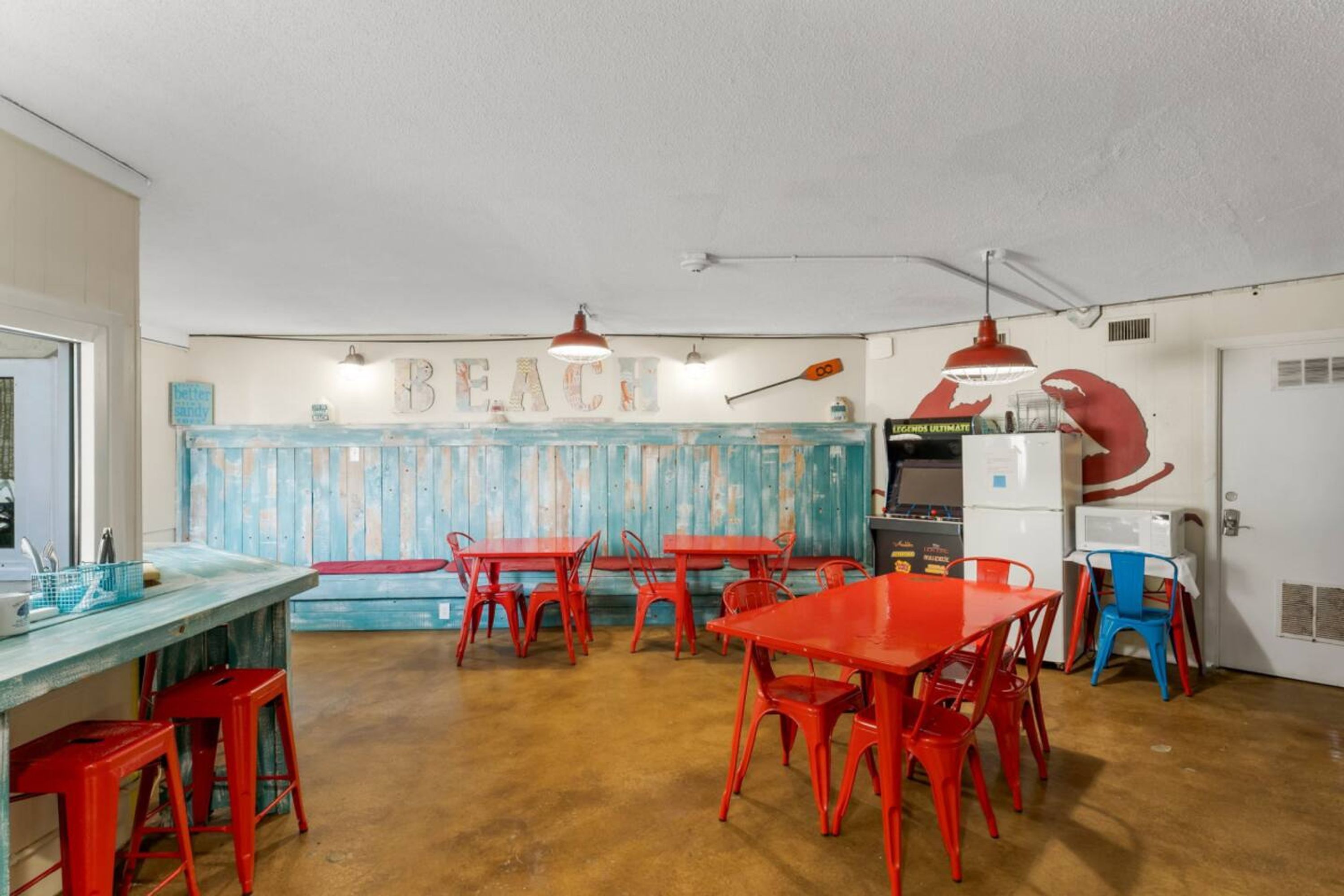 A kitchen with red chairs, a blue table, and a wall with the word 'BEACH' painted on it.