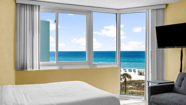 Quarto de hotel com uma janela grande que oferece vista para a praia e o oceano.