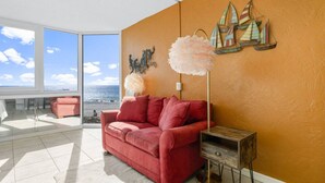 A modern living room with a red sofa, a small wooden side table, and a large window offering a view of the sea. - Top of the Gulf 421 - Luxury Beach View Condo (Panama City Beach)
