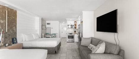 Una habitación de hotel moderna con una cama grande, un sofá, un televisor y una kitchenette al fondo.