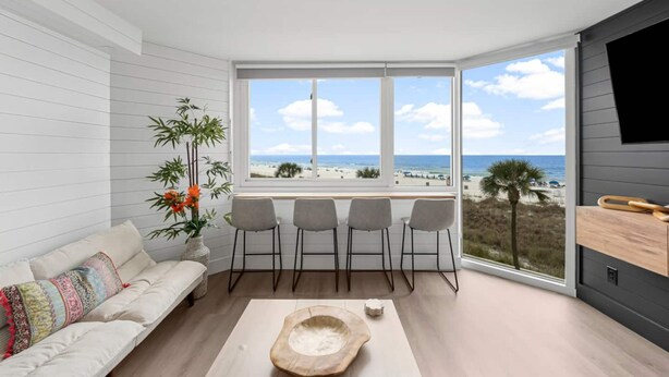 A modern living room with a view of the beach, a sofa, chairs, and a wooden bowl on the floor.