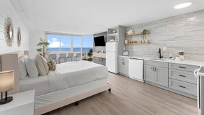 A modern bedroom with a large bed, a desk, and a view of the ocean.