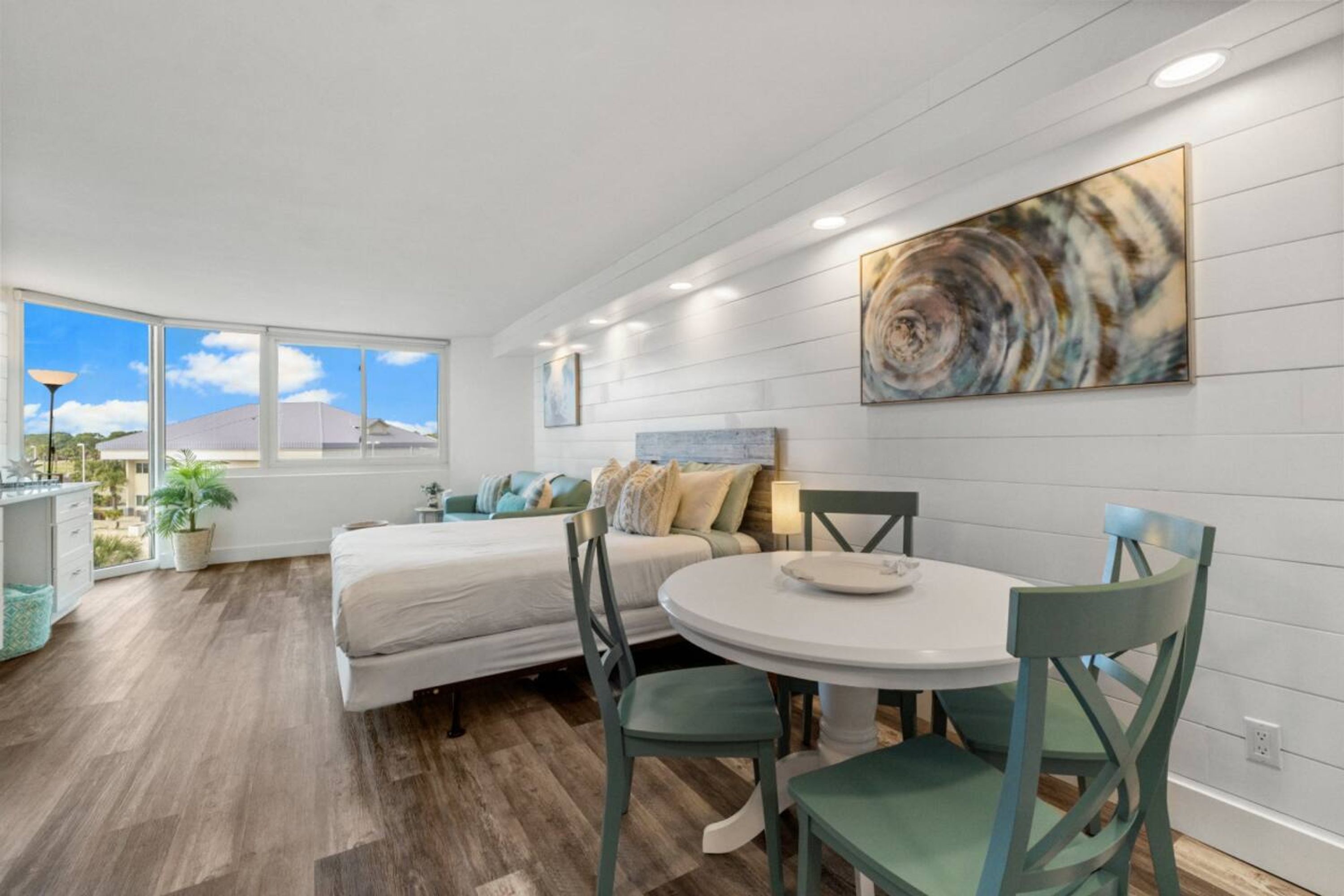 A modern bedroom with a large window, a bed, a bedside table, and a dining area with a table and chairs.