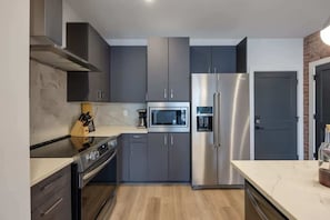 A modern kitchen with grey cabinets, stainless steel appliances, and a marble countertop.