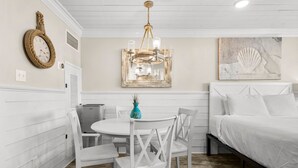 A room with a bed, a dining table with chairs, a chandelier, a clock, and a framed picture on the wall. - Beachfront Studio Condo - Top of the Gulf 317 (Panama City Beach)