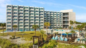 A multi-story hotel with a modern design, featuring balconies and a pool area with lounge chairs. - Beachfront Studio Condo - Top of the Gulf 317 (Panama City Beach)