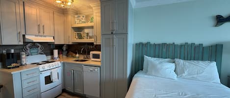 Et kompakt hotelværelse med tekøkken, seng med hvide sengetøj og en grønlig sengegavl.