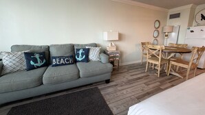 A cozy room with a grey sofa, a small wooden table, and a bed. - Renovated Beach Front Condo - Top of the Gulf 302 (Panama City Beach)