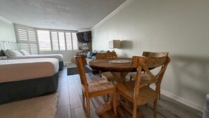 A cozy bedroom with a bed, a wooden dining table with chairs, and a small kitchenette area. - Renovated Beach Front Condo - Top of the Gulf 302 (Panama City Beach)