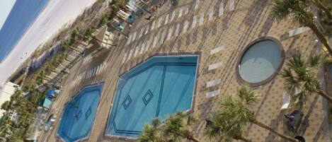 Un espace piscine comprenant plusieurs piscines, des palmiers et une allée dallée.