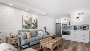 A modern living room with a grey sofa, wooden coffee table, and a kitchen area with white cabinets and a built-in oven. - Summit 808 - Luxury Beach Resort Condo 1-6 People (Panama City Beach)