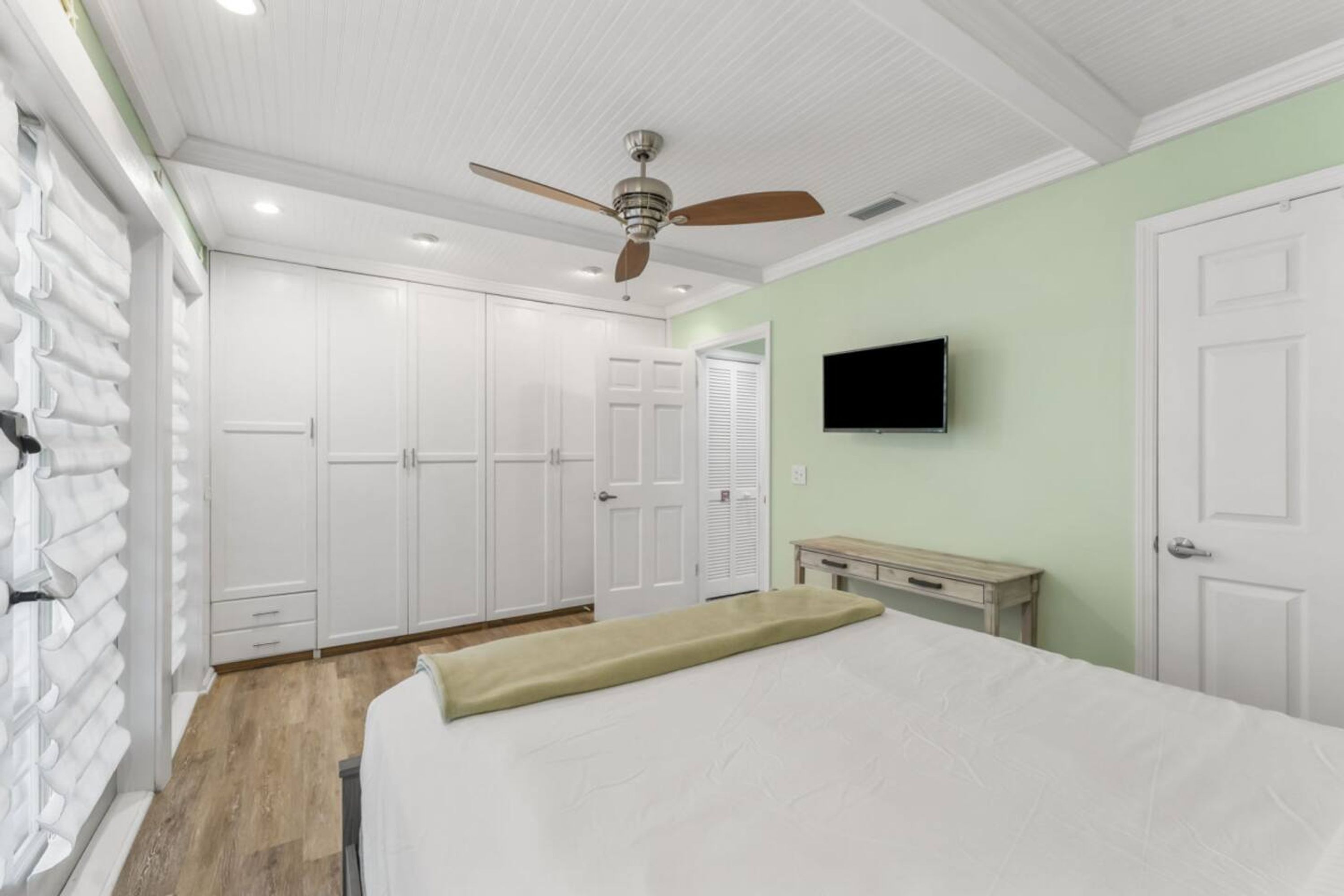 A bedroom with a bed, a ceiling fan, a TV mounted on the wall, and a wardrobe.