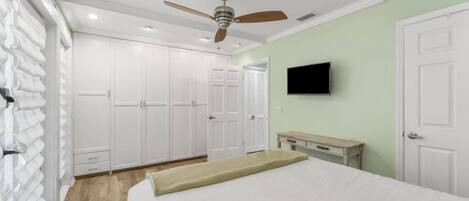 A bedroom with a bed, a ceiling fan, a TV mounted on the wall, and a wardrobe.