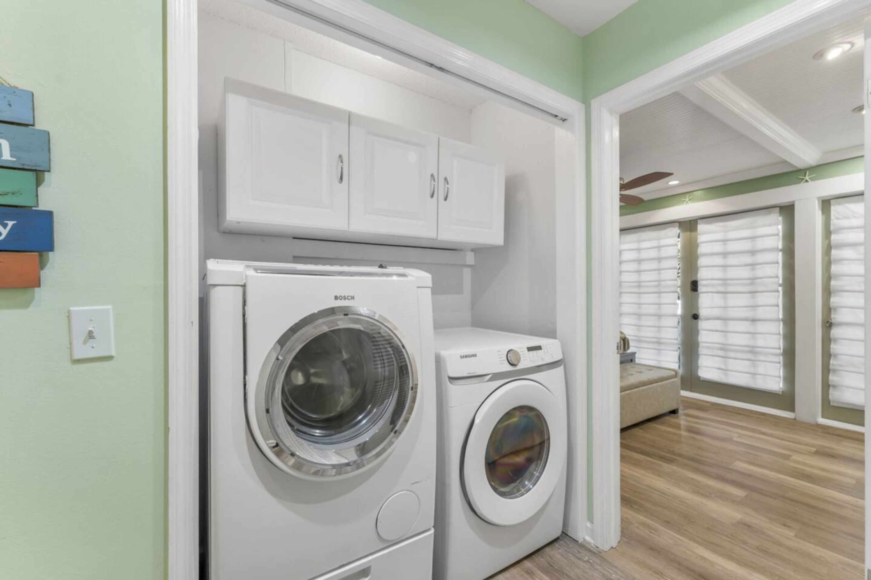 A laundry room with Bosch and Samsung washing machines, white cabinets, and a bench.
