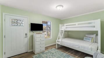 Une chambre avec un lit superposé, une commode, un téléviseur et une fenêtre avec des stores.