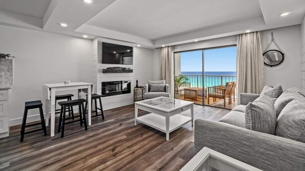 A modern living room with a wooden floor, a white coffee table, a grey sofa, and a dining area with a white table and black stools.