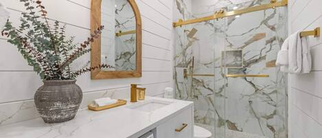 A modern bathroom with a marble shower, a wooden-framed mirror, and a white sink.