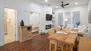 A modern, well-lit living room with a wooden dining table, white sofas, and a fireplace.