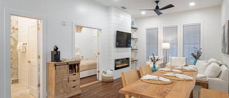 A modern, well-lit living room with a wooden dining table, white sofas, and a fireplace.