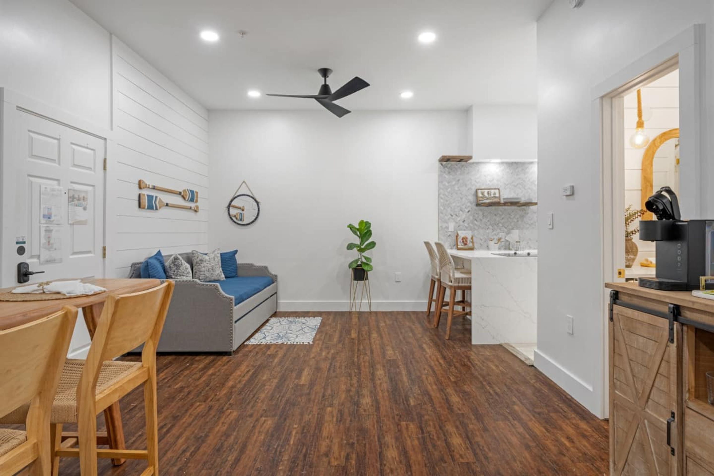 Una sala de estar moderna con sofá, mesa de comedor y sillas. Cuenta con una zona de cocina con mostrador y armarios.